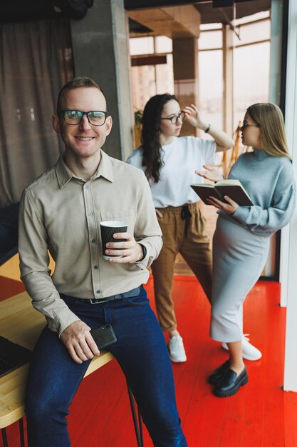 Young confident business people standing in an office space with a group of colleagues in the background working on a laptop computer The work of colleagues in a modern office