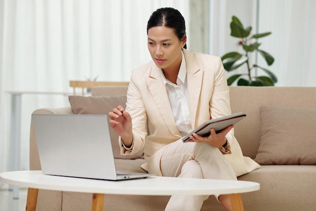 Young confident chief executive office with tablet looking at laptop screen