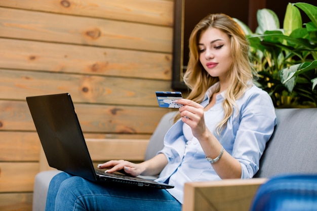 Photo young confident pretty caucasian woman working with laptop and credit card, sitting on the sofa