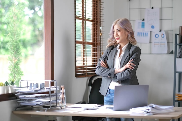 Young confident smiling Asian business woman leader successful entrepreneur elegant professional company executive ceo manager Asian business woman is standing in office with arms crossed