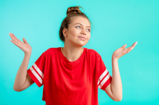 Young confused woman in fashion red t-shirt with arms out shrugs shoulders