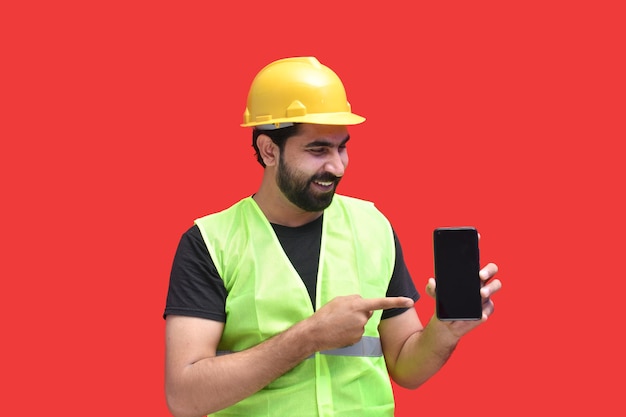 young construction worker smiling holding phone and pointing it indian pakistani model