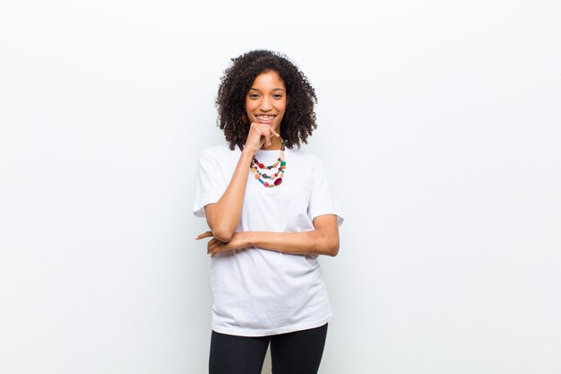 Young cool african american woman looking happy and smiling with hand on chin, wondering or asking a question, comparing options