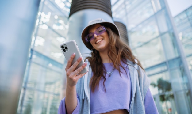 Young cool girl holding and using mobile phone smiling woman texting with friends high quality photo