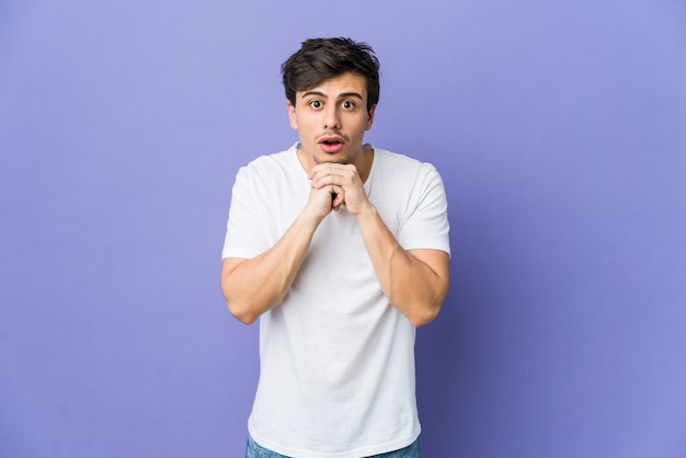 Young cool man praying for luck, amazed and opening mouth looking to front.