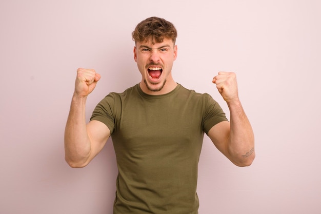 Young cool man shouting aggressively with an angry expression or with fists clenched celebrating success