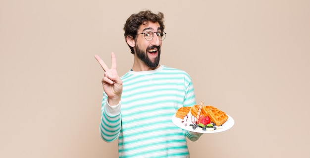 Young cool man with waffles against flat wall.