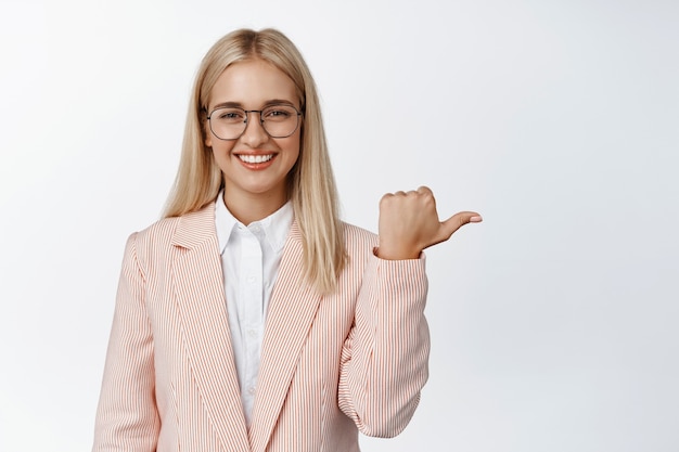 Young corporate woman, professional saleswoman in glasses and suit, pointing finger right on white.