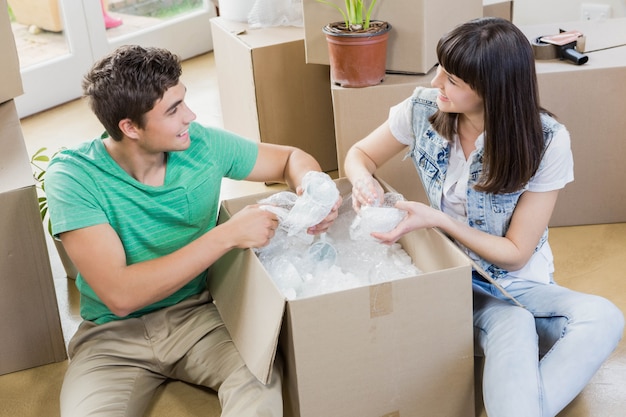 Young couple assisting each other while unpacking carton boxes in new house