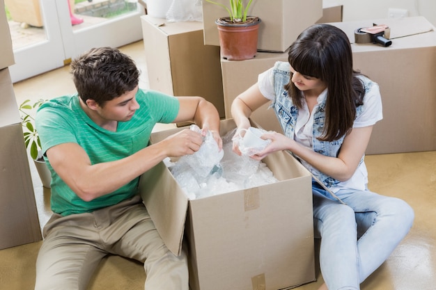 Young couple assisting each other while unpacking carton boxes in new house