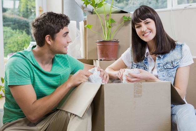 Young couple assisting each other while unpacking carton boxes in new house