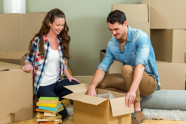 Young couple assisting each other while unpacking carton boxes in new house