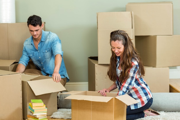 Young couple assisting each other while unpacking carton boxes in new house