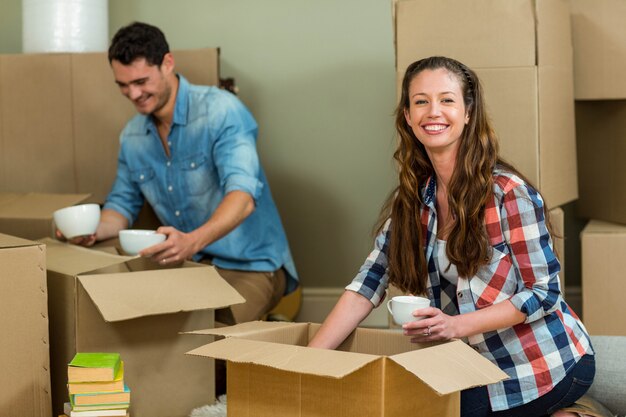 Young couple assisting each other while unpacking carton boxes in new house