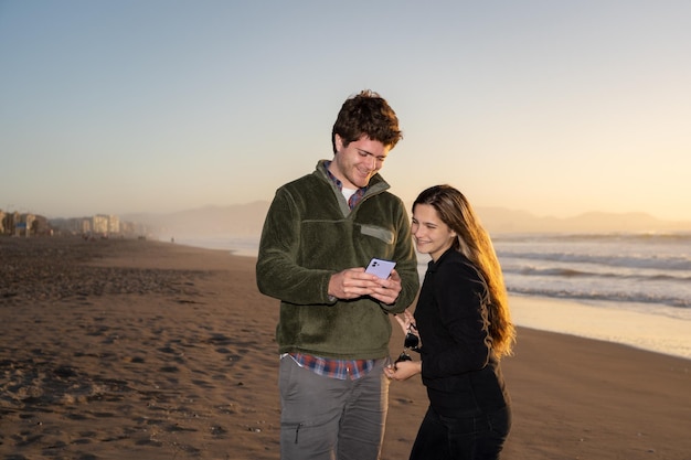 young couple on the beach looking at cellphone or mobile device and smiling on the beach