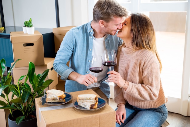 Young couple celebrating buying new house while drinking wine on cardboard