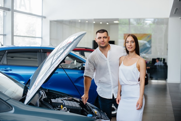 A young couple chooses a new car at the dealership and consults with a representative of the dealership. Used cars for sale. Dream fulfillment.