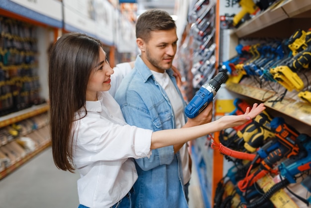 Young couple choosing instrument in hardware store.