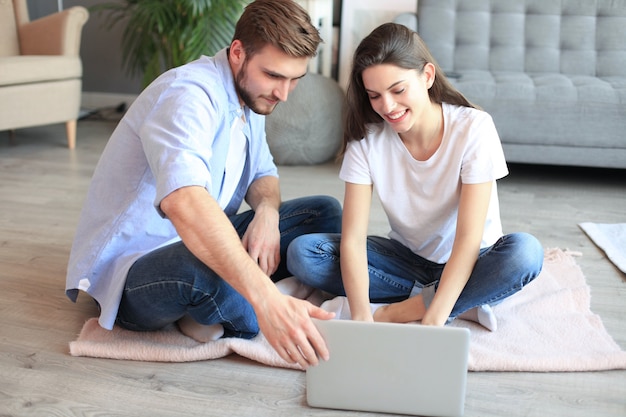 Young couple doing some online shopping at home, using a laptop on floor.