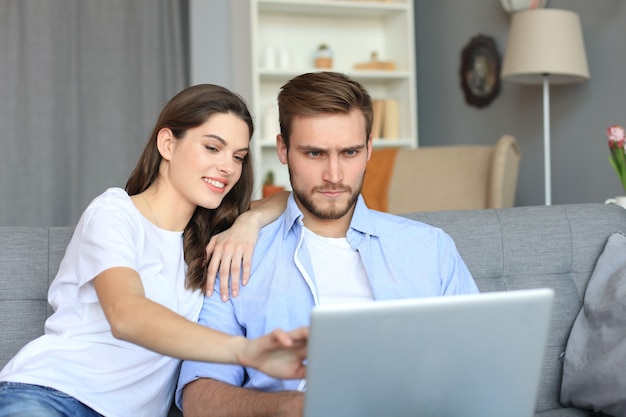 Young couple doing some online shopping at home, using a laptop on the sofa.