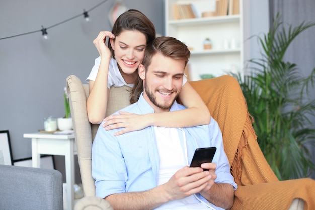 Young couple doing some online shopping at home, using smart phone on the sofa.