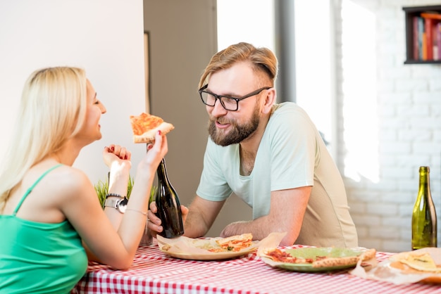 Young couple dressed casually having a lunch with pizza and beer at home