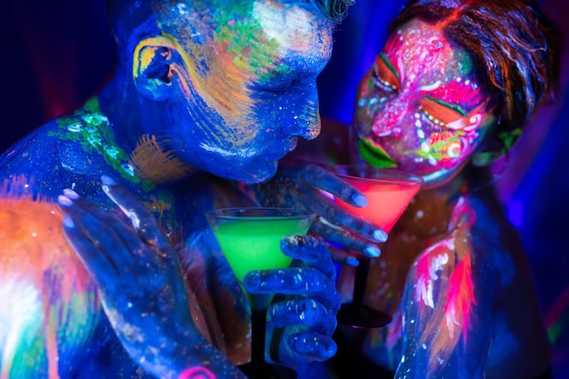 Young couple drink an alcoholic drink in a nightclub Man and woman with fluorescent bodyart