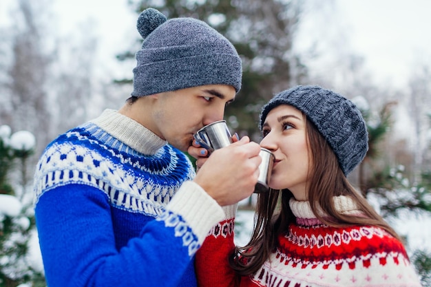 Young couple drinking tea in winter forest Happy people relaxing outdoors during holidays