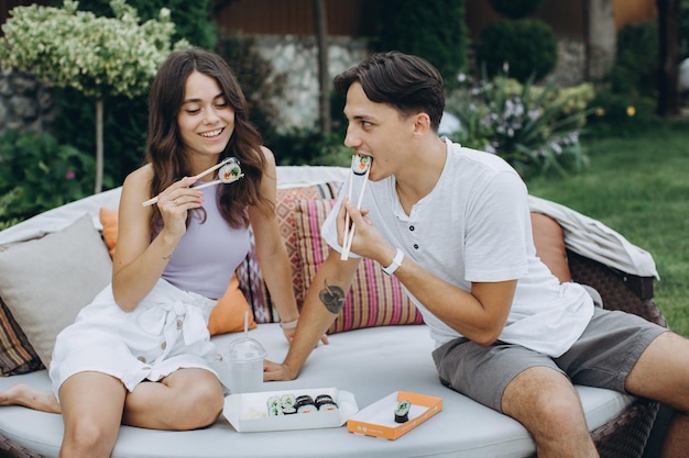 Young couple eating sushi sitting outdoors