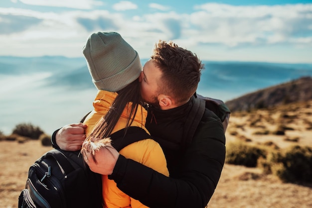 A young couple embracing standing on top of a mountain