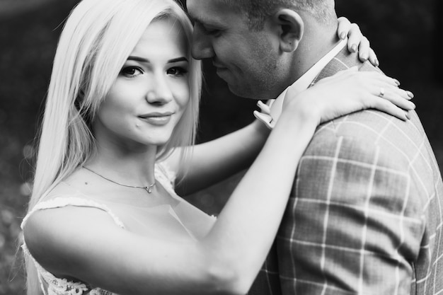 Young couple enjoying romantic moments while walking in the park. Stylish bride and groom posing and kissing in the park on their wedding day. Elegant bride in beautiful white dress, groom in a suit.