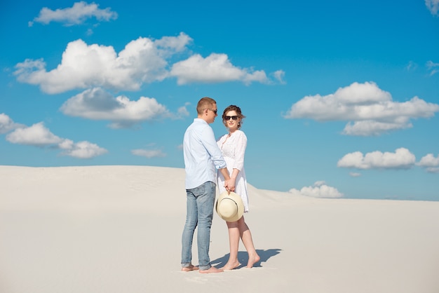 Young couple enjoying the sunset in the dunes. Romantic traveler walks in the desert. Adventure travel lifestyle concept