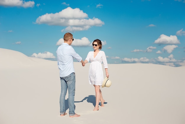 Young couple enjoying the sunset in the dunes. Romantic traveler walks in the desert. Adventure travel lifestyle concept