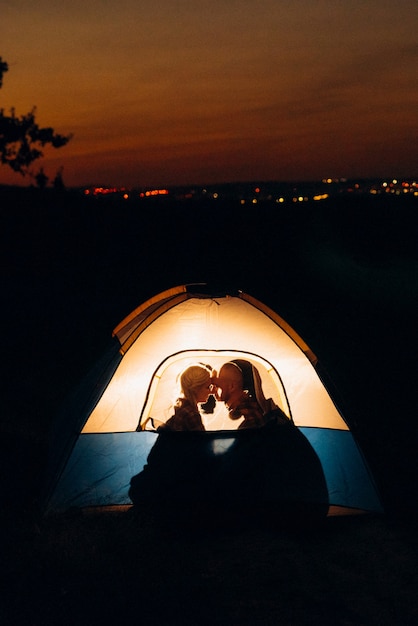 Young couple a guy and a girl in bright knitted hats stopped at a camping near the fire