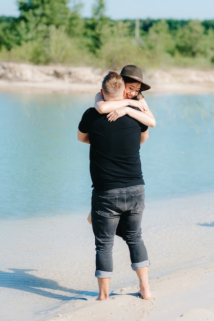 Young couple a guy with a girl in black clothes are walking on the white sand at the edge of blue water