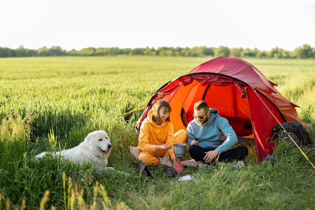 Young couple have a picnic with a dog near the tent on greenfield