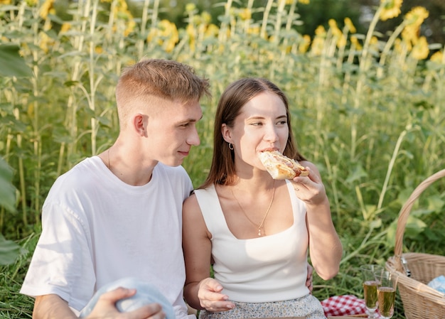 Young couple having picnic on sunflower field at sunset