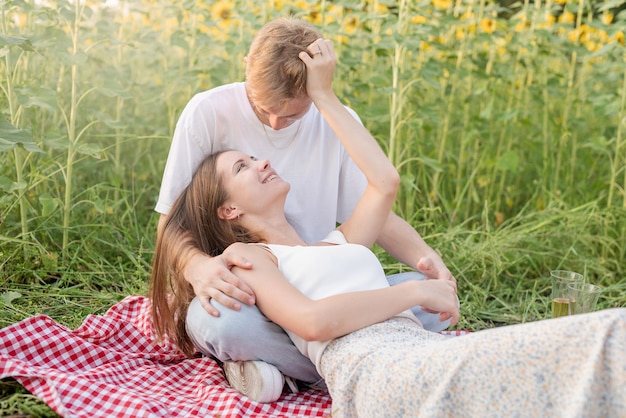 Young couple having picnic on sunflower field at sunset