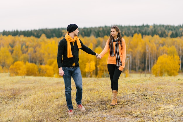 A young couple holding hands on a colorful autumn background.