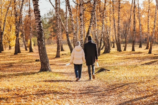 Young couple holding hands walking in autumn park holding disposable medical masks in their hands