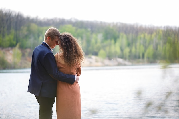 A young couple holding hands on a wooden bridge in the middle of a blue lake. Masonry on the island on a background of trees. Nature, landscape. Romance and love, happy couple