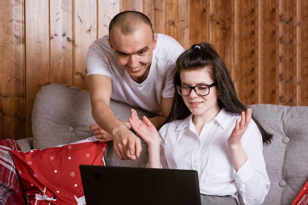 A young couple at home sitting on the couch communicating online via laptop with relatives