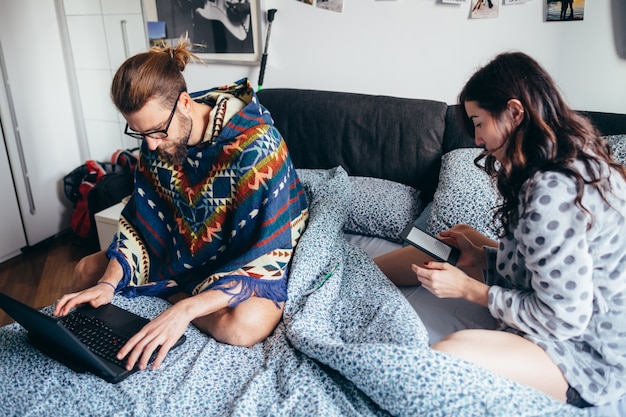 Young couple indoor at home sitting bed using computer and ebook