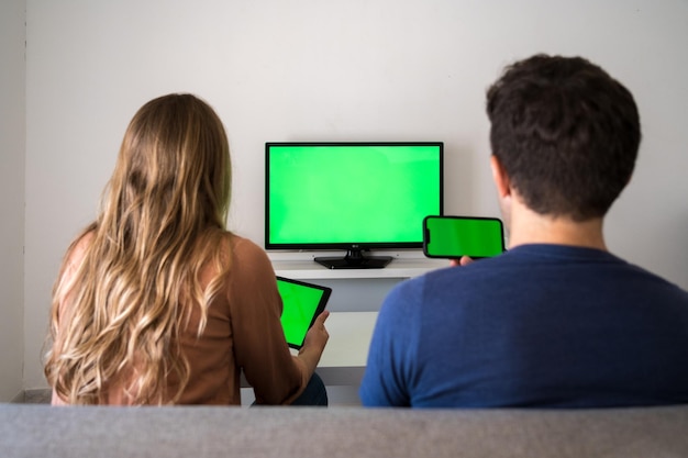 Young couple is sitting on the couch at home with a tablet. Green screen