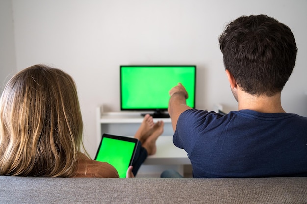 Young couple is sitting on the couch at home with a tablet. Green screen