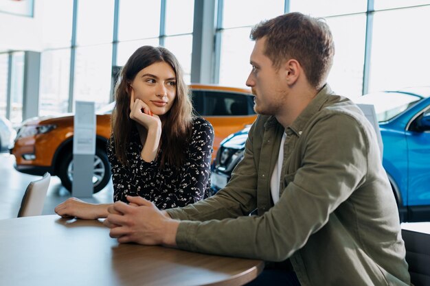 A young couple is sitting at a table in a dealership and waiting for a sales manager Buying a new family car