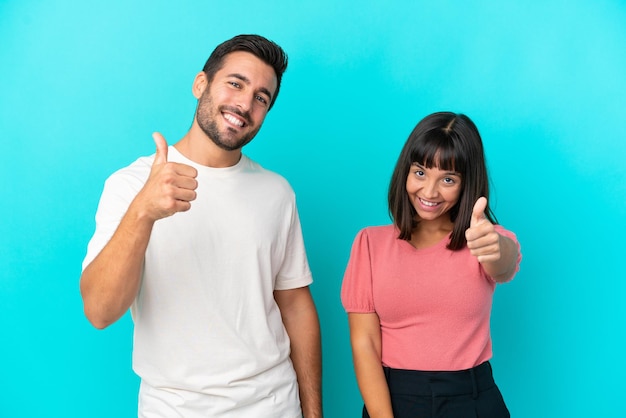 Young couple isolated on blue background giving a thumbs up gesture because something good has happened