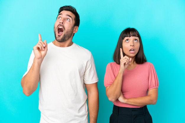 Young couple isolated on blue background thinking an idea pointing the finger up