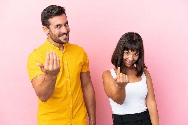 Young couple isolated on pink background inviting to come with hand Happy that you came