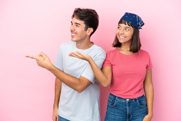 Young couple isolated on pink background pointing back and presenting a product